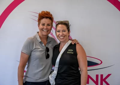 A woman with short red hair smiles for a photo with a woman wearing a black golfing tank top and sunglasses