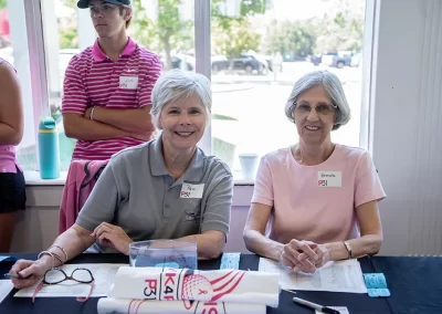 Two older women with short, grey hair sit behind a table