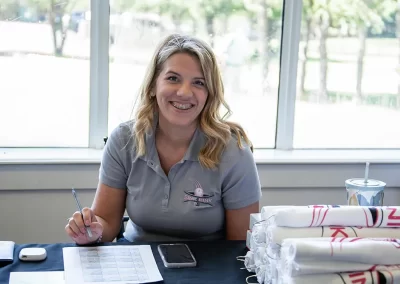 A younger woman with blonde hair and braces holds a pen while sitting at a table