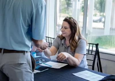 A women with red hair in a grey polo hands a man a business card