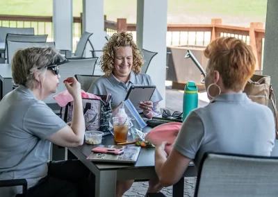 Three women wearing grey polos eat lunch and chat