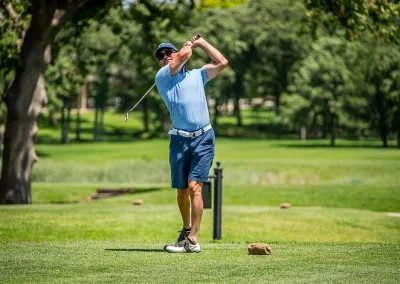 A man wearing a blue polo hits a golf ball