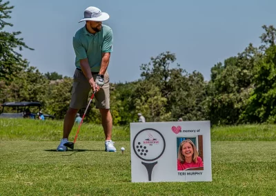 A man wearing a grey hat and teal polo hitting a golf ball