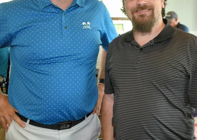 A man in a blue shirt with spots poses with a man wearing a gray striped shirt