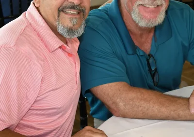 Man in a pink shirt and man in a teal shirt sit at a table in the club house