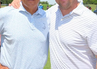 One man with a striped shirt has an arm around a man with a blue shirt on the golf course