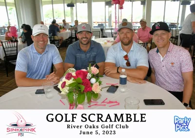 For men sitting at a table in the club house. Three are wearing blue, and one is in pink