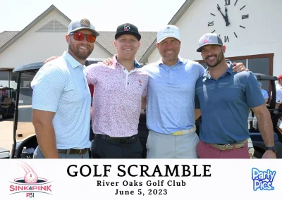 Four white men smiling in front of the club house clock outdoors with their arms around each other