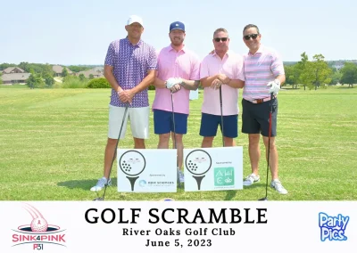 Four men on the golf course with their clubs. The two in the middle are wearing pink. The one on the left is wearing pink and purple, and the one on the right has pink stripes.