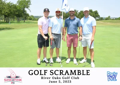 Four younger men wearing pastel polos and hats smile in front of a golf course flag