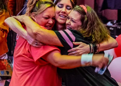 Three women wearing colorful costumes smile and hug