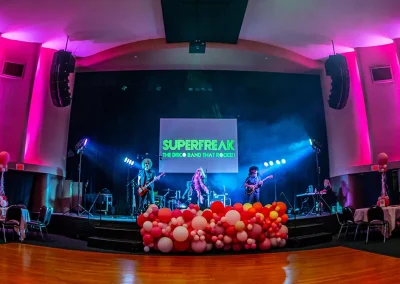 Disco rock band performing on stage at indoor breast cancer awareness event