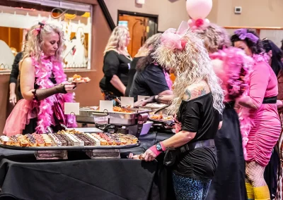 Two women wearing retro costumes put desserts from a table spread on their plates