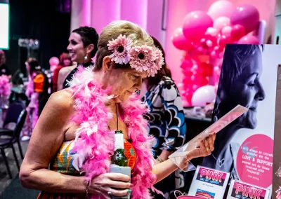 An older woman wearing a pink flower crown and pink feature boa holds and reads a sign in her hand