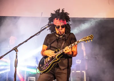 A middle-aged man wearing a black vest and black jeans plays the guitar