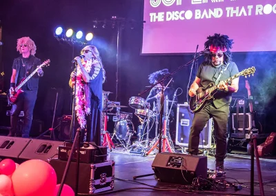 A female lead singer sings on stage as two middle-aged men play guitar next to her