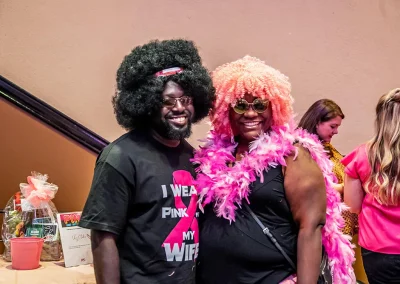 A couple wearing fake afro wigs pose in front of a raffle table