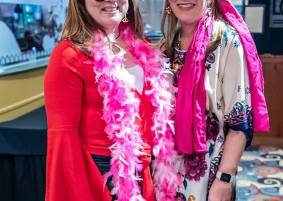 Two middle-aged women wearing sunglasses smile and pose for a photo at an indoor event