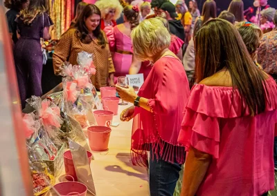 An older woman wearing pink holds a wine glass and puts a raffle ticket in a pink bucket