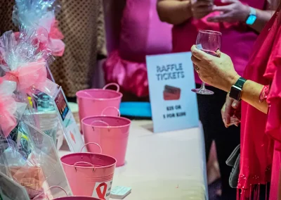 A woman wearing pink holds a glass of wine next to raffle ticket buckets