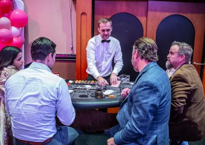 A young couple and two middle-aged men play card games at a table with a male croupier