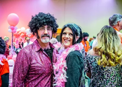 An older couple wearing 70s costumes smile for a photo