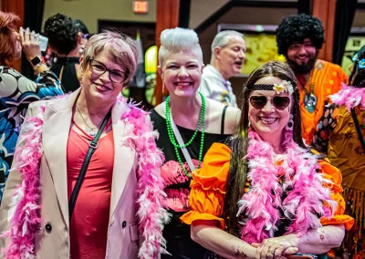 Three older women wearing bright costumes smile for a photo