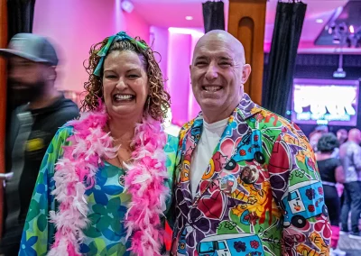 A woman with a pink feather boa smiles next to a man in a rainbow patterned jacket