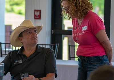 A Project31 team member talks with an older man wearing a cowboy hat. He is eating lunch at the Sink4Pink golf tournament.