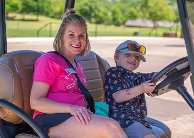 A Project31 team member smiles while sitting passenger side in a golf cart. A young boy holds the steering wheel and pretends to drive.