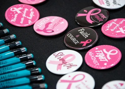 A collection of pink and black breast cancer support buttons and blue pens.