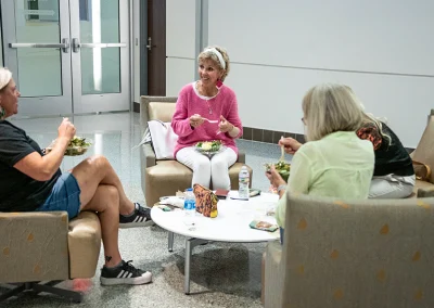 Three older women sit in green linen chairs and chat with one another in the lobby at the breast cancer survivorship expo.