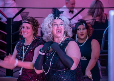 Three women smiling and dancing while wearing 1920s costumes at the Paint the Town Pink Gala.