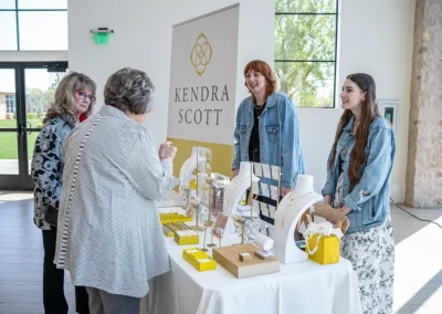 Employees from Kendra Scott talk with two women at their promotional table at the Proton Luncheon