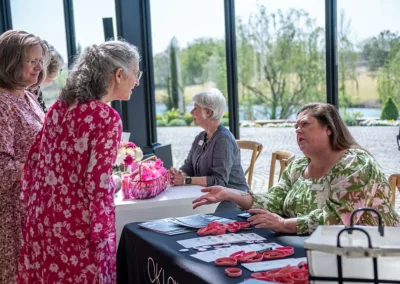 A woman wearing a pink dress talks to another woman sitting behind a table