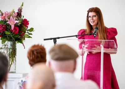 A woman in a pink dress gives a speech at the podium.