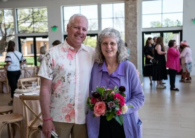 A husband and wife pose for a photo. The wife is holding a bouquet.